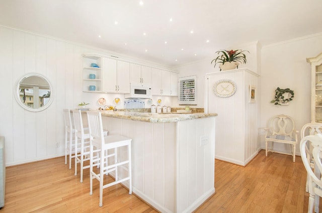 kitchen with white cabinets, kitchen peninsula, light wood-type flooring, and light stone counters