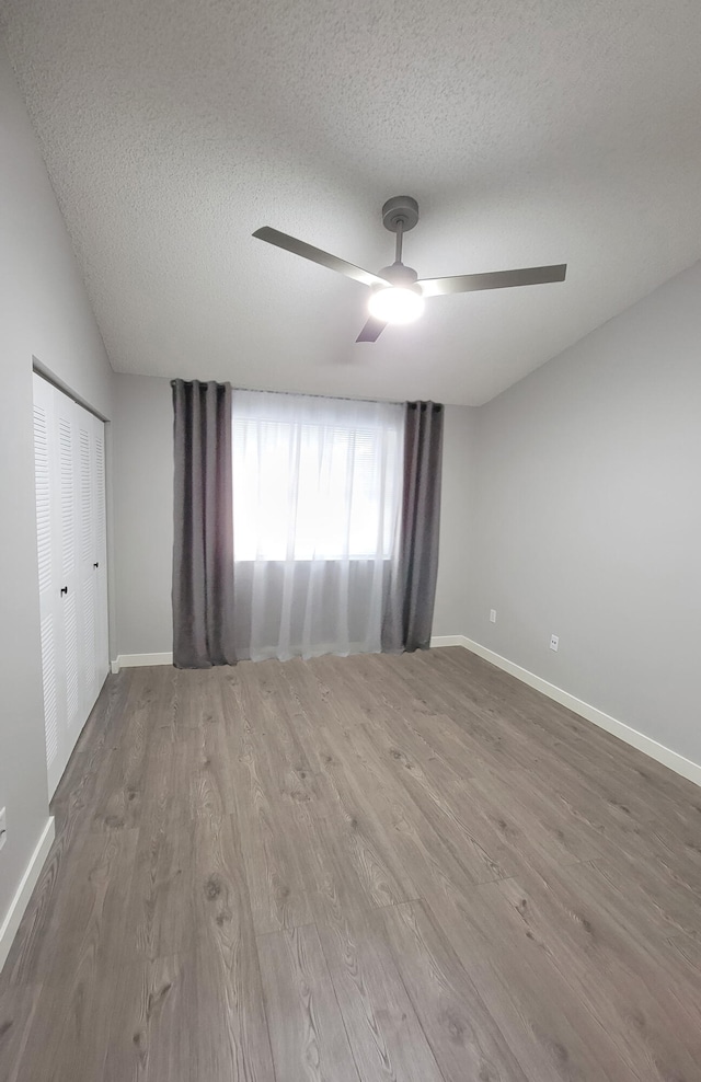 empty room featuring wood-type flooring, ceiling fan, vaulted ceiling, and a textured ceiling