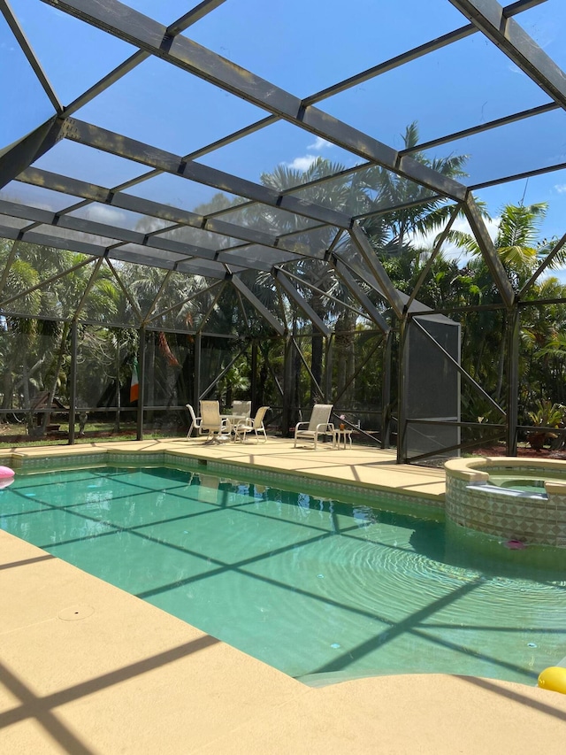 view of pool with a patio, glass enclosure, and an in ground hot tub