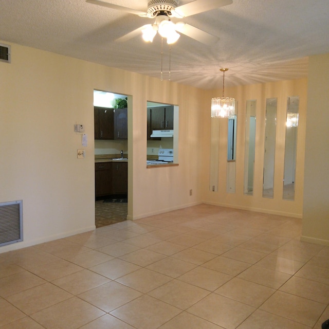 empty room with a textured ceiling, light tile patterned floors, ceiling fan with notable chandelier, and sink