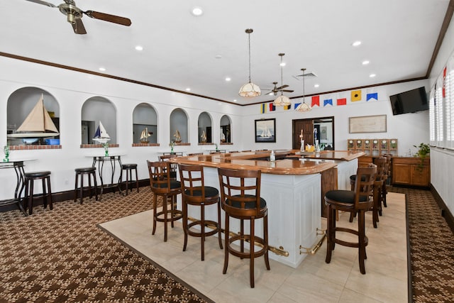 interior space featuring decorative light fixtures, ceiling fan, a kitchen island with sink, a kitchen breakfast bar, and light tile floors