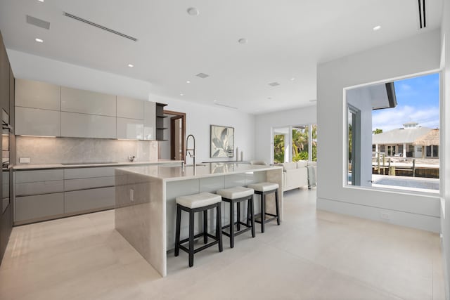 kitchen with backsplash, gray cabinets, light tile floors, and a breakfast bar area