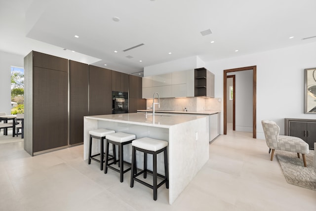 kitchen featuring light tile floors, a breakfast bar, black double oven, a kitchen island with sink, and sink