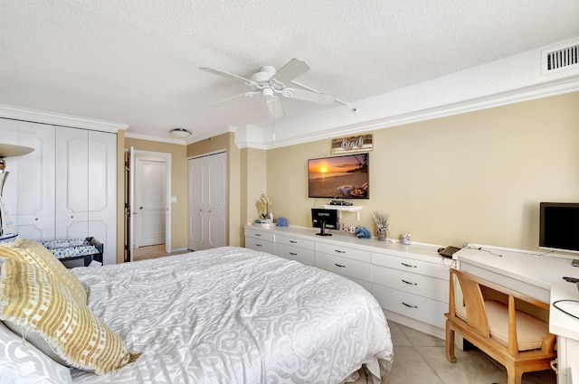 bedroom with a textured ceiling, ceiling fan, crown molding, light tile patterned floors, and multiple closets