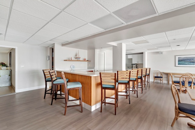 bar with a drop ceiling, white cabinets, and wood-type flooring