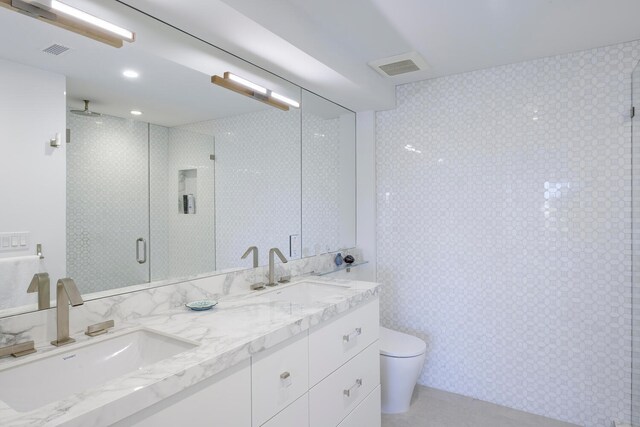 bathroom with tile flooring, a shower with shower door, double vanity, and toilet