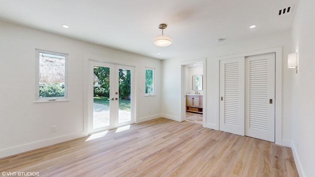 unfurnished bedroom featuring french doors, light wood-type flooring, ensuite bath, access to outside, and a closet