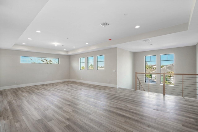 empty room with plenty of natural light, a raised ceiling, and light wood-type flooring