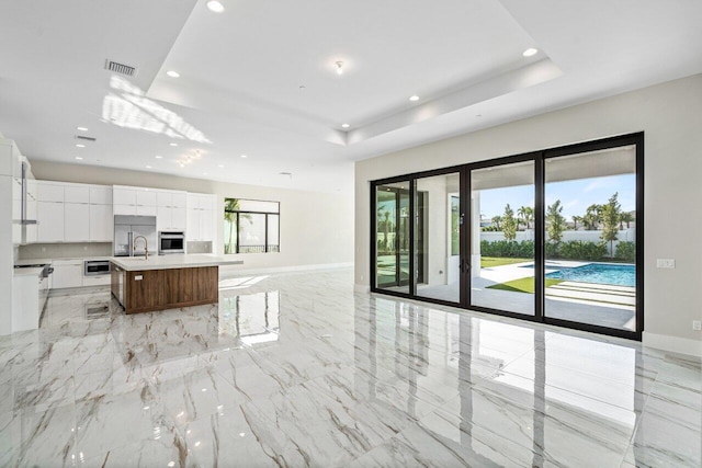 kitchen with a spacious island, stainless steel oven, a raised ceiling, and white cabinets