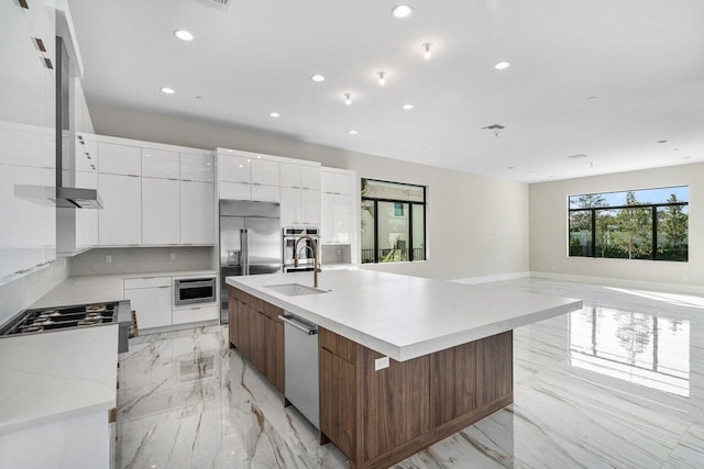 kitchen featuring sink, white cabinets, built in appliances, wall chimney range hood, and a spacious island