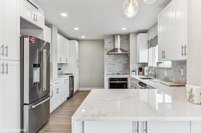 kitchen featuring appliances with stainless steel finishes, light wood-type flooring, light stone counters, wall chimney range hood, and tasteful backsplash