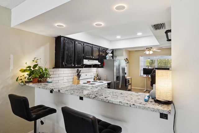 kitchen with electric stove, kitchen peninsula, ceiling fan, a kitchen breakfast bar, and backsplash