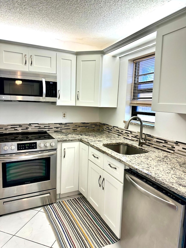 kitchen with white cabinetry, stainless steel appliances, sink, and light stone counters