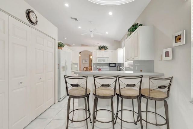 kitchen with white appliances, light tile patterned floors, vaulted ceiling, white cabinets, and kitchen peninsula