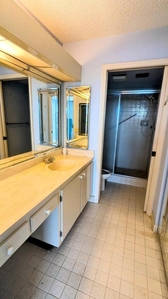 bathroom with tile patterned flooring, a textured ceiling, toilet, vanity, and a shower with shower door