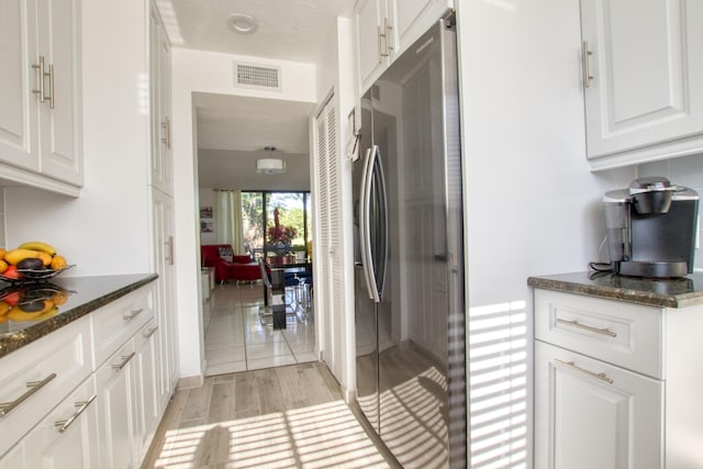 kitchen featuring stainless steel fridge, dark stone countertops, light tile floors, and white cabinetry