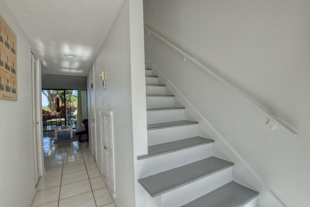 stairway with a textured ceiling and light tile flooring