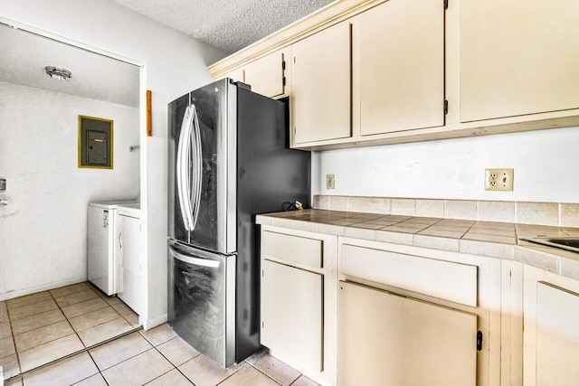 kitchen featuring stainless steel fridge, a textured ceiling, cream cabinetry, washing machine and dryer, and light tile patterned flooring