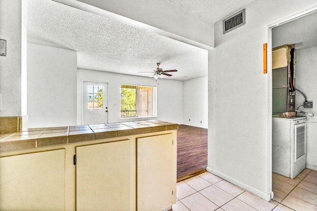 kitchen with ceiling fan, tile counters, a textured ceiling, and light hardwood / wood-style flooring