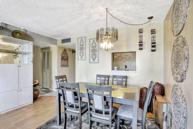 dining space featuring a notable chandelier, a textured ceiling, and light hardwood / wood-style flooring