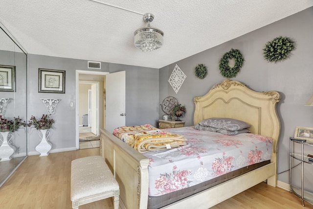 bedroom featuring a textured ceiling, a chandelier, and light hardwood / wood-style flooring