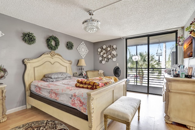 bedroom featuring an inviting chandelier, light wood-type flooring, access to outside, a textured ceiling, and floor to ceiling windows