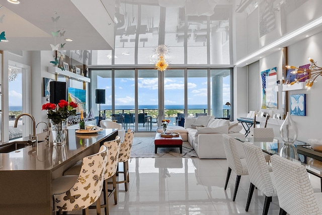 dining space featuring a chandelier, light tile flooring, expansive windows, a towering ceiling, and sink