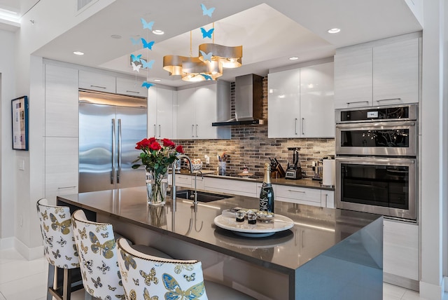 kitchen featuring a kitchen breakfast bar, appliances with stainless steel finishes, sink, light tile floors, and wall chimney exhaust hood