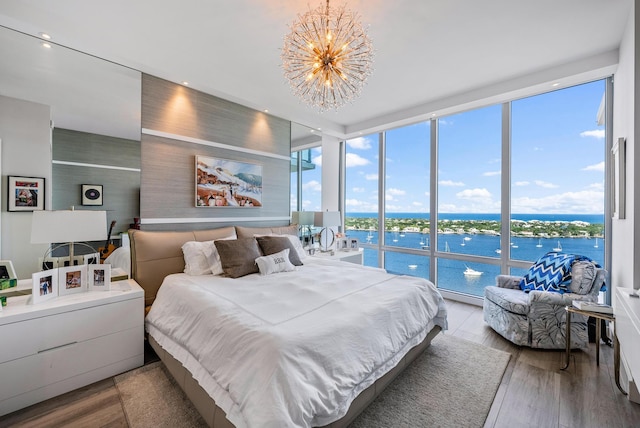 bedroom featuring expansive windows, multiple windows, light hardwood / wood-style flooring, a water view, and a chandelier