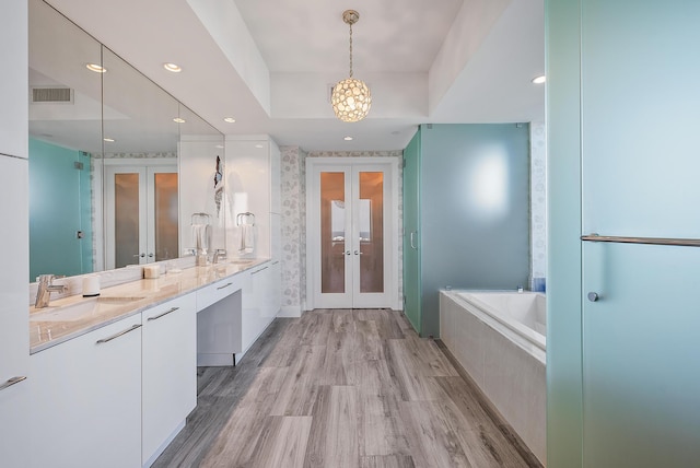 bathroom featuring double sink vanity, a bath to relax in, a raised ceiling, french doors, and hardwood / wood-style flooring