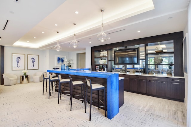 bar with decorative light fixtures, dark brown cabinets, and a tray ceiling