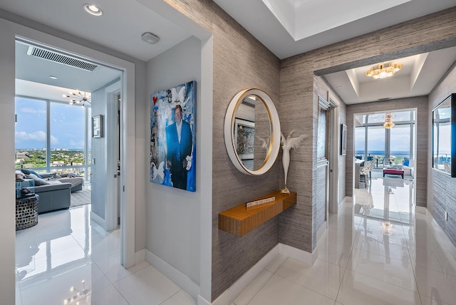 hall featuring a tray ceiling, light tile floors, and an inviting chandelier