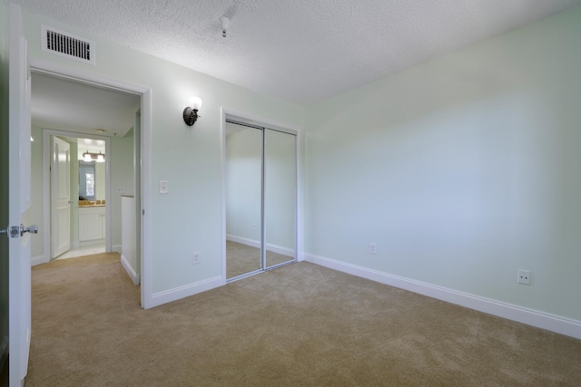 unfurnished bedroom with light carpet, a closet, and a textured ceiling