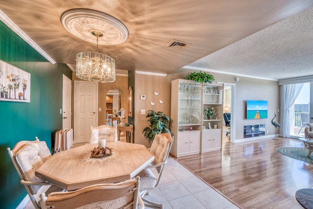 dining room with a chandelier, a textured ceiling, light wood-type flooring, and crown molding