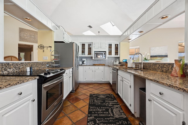 kitchen featuring lofted ceiling with skylight, white cabinets, stainless steel appliances, backsplash, and sink