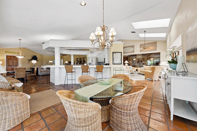 dining area featuring lofted ceiling with skylight, dark tile flooring, and ceiling fan with notable chandelier