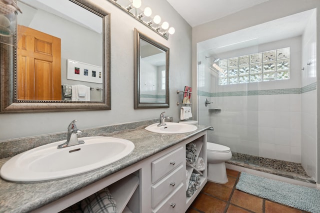 bathroom featuring toilet, oversized vanity, double sink, tile flooring, and a tile shower