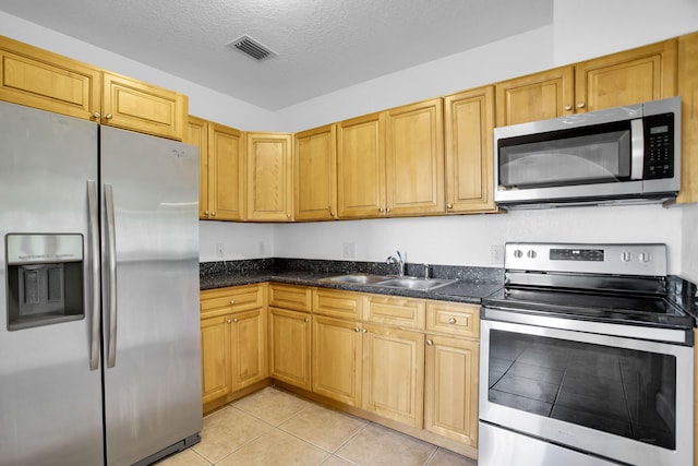 kitchen featuring appliances with stainless steel finishes, a textured ceiling, sink, light tile flooring, and dark stone counters