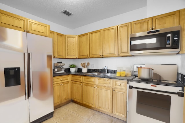 kitchen with appliances with stainless steel finishes, a textured ceiling, sink, and light tile flooring