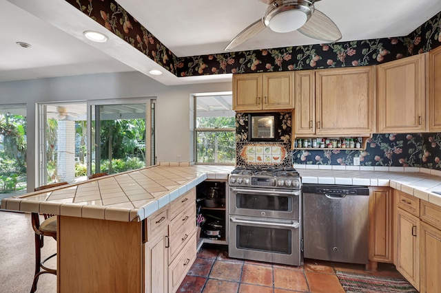 kitchen featuring tile counters, ceiling fan, appliances with stainless steel finishes, and dark tile flooring