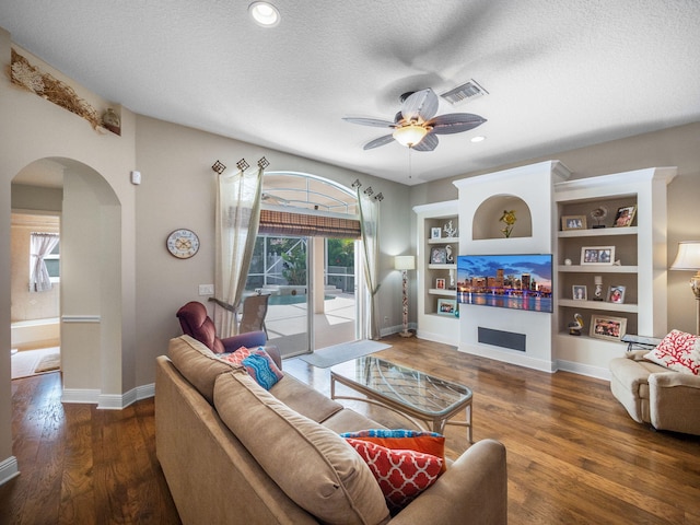 living room featuring ceiling fan, built in features, dark wood-type flooring, and a textured ceiling