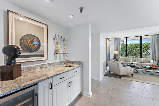 bar with sink, white cabinetry, light stone countertops, light tile patterned flooring, and beverage cooler