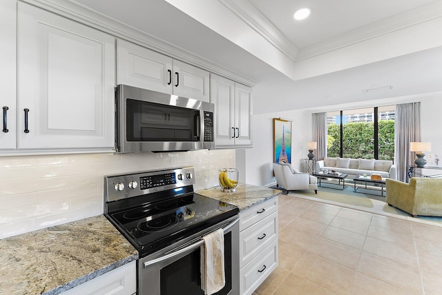 kitchen featuring stone counters, light tile patterned flooring, appliances with stainless steel finishes, white cabinets, and ornamental molding