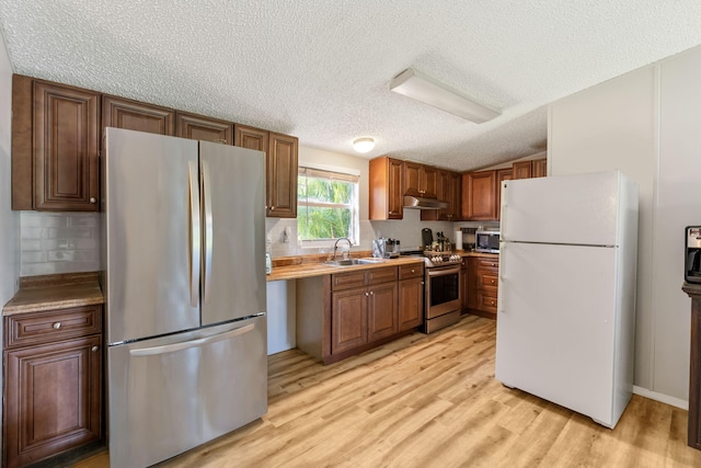 kitchen with sink, stainless steel appliances, tasteful backsplash, a textured ceiling, and light wood-type flooring