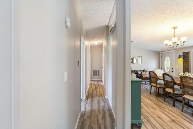 corridor featuring light hardwood / wood-style flooring, a textured ceiling, and an inviting chandelier