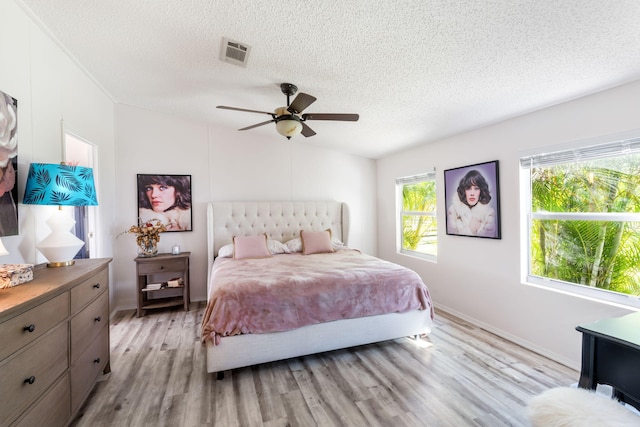 bedroom with multiple windows, a textured ceiling, ceiling fan, and light wood-type flooring