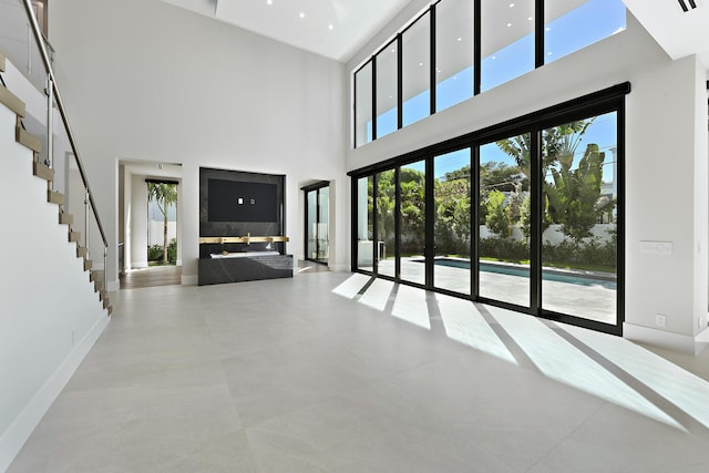 unfurnished living room featuring plenty of natural light, light tile floors, and a towering ceiling