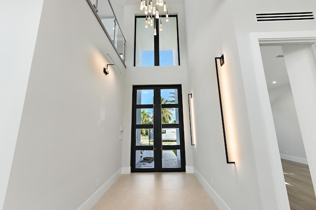 doorway to outside featuring a chandelier, a towering ceiling, light hardwood / wood-style flooring, and french doors