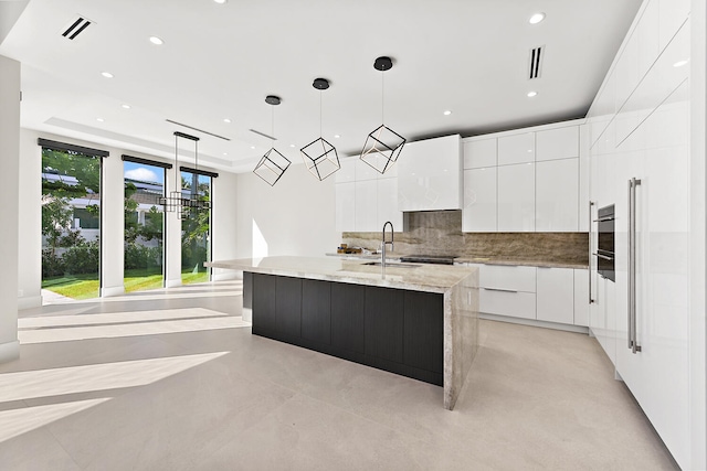 kitchen featuring tasteful backsplash, white cabinets, pendant lighting, and a center island with sink