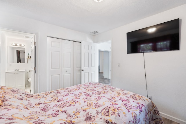 bedroom with a textured ceiling, wood-type flooring, a closet, and ensuite bath